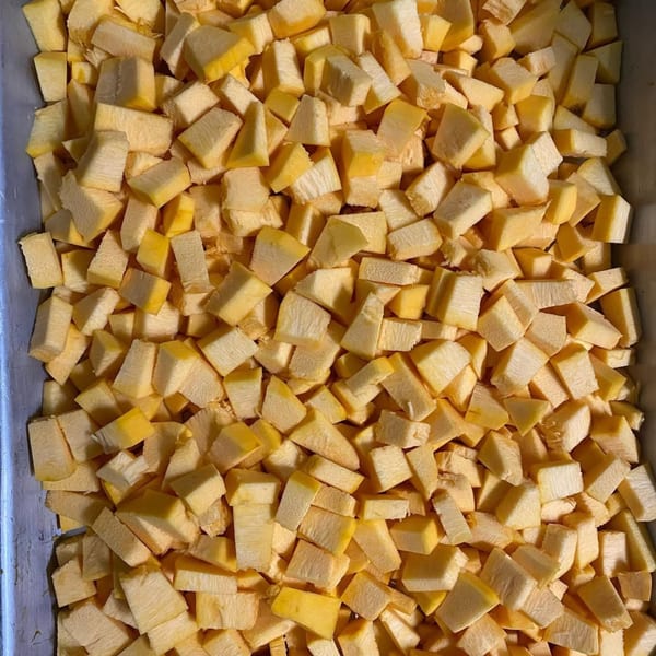 Close-up overhead view of a large quantity of diced yellow squash or pumpkin pieces.