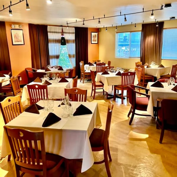 The Bete-Lukas dining room features set tables with white cloths, dark chairs, and warm lighting.