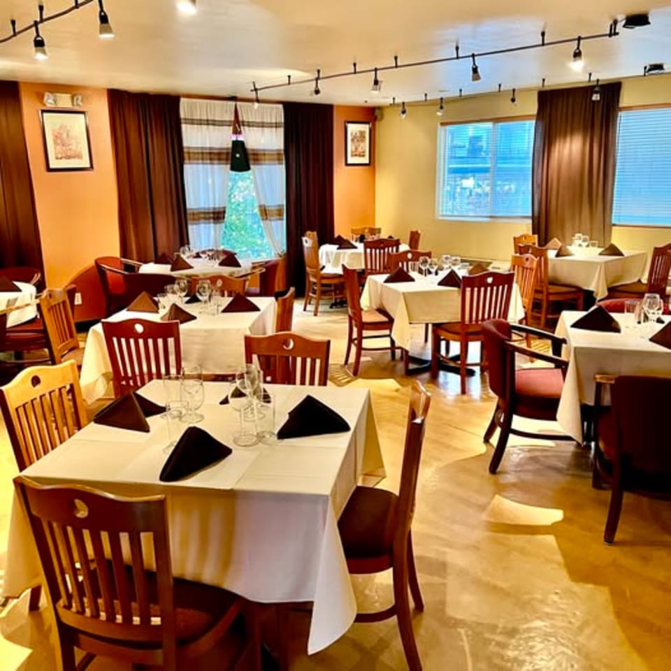 The Bete-Lukas dining room features set tables with white cloths, dark chairs, and warm lighting.