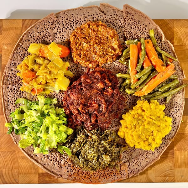 A large platter of Ethiopian injera bread topped with various colorful stews and vegetables.
