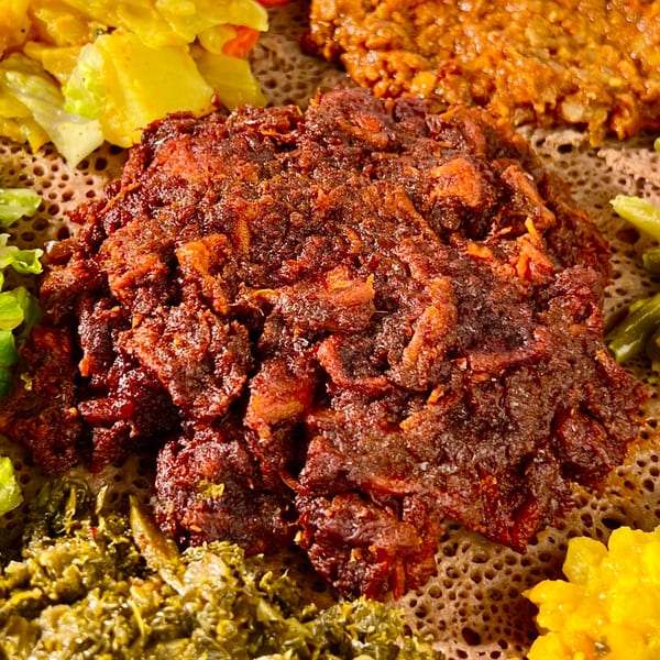 Close-up of Ethiopian kitfo, a minced meat dish, surrounded by colorful vegetable stews on injera bread.