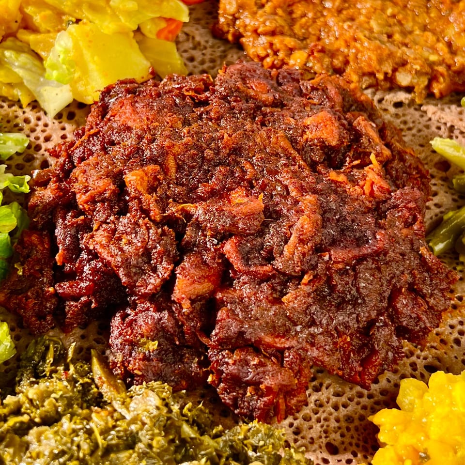 Close-up of Ethiopian kitfo, a minced meat dish, surrounded by colorful vegetable stews on injera bread.