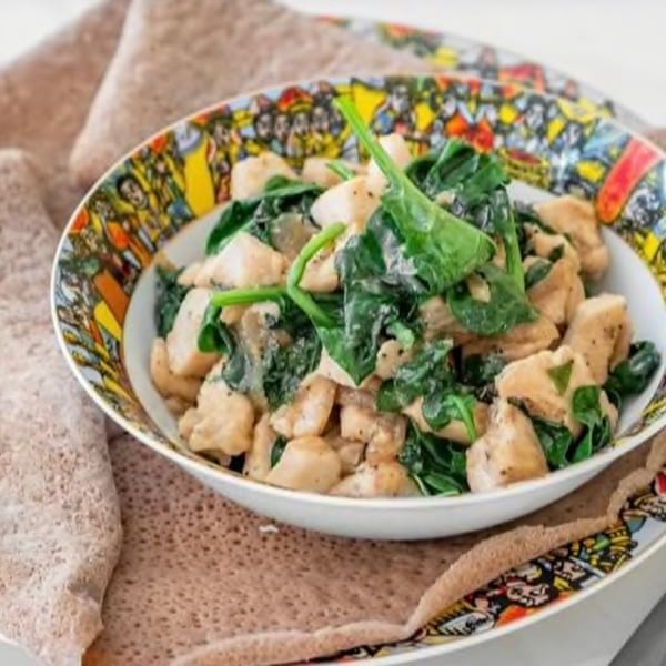 Ethiopian chicken and spinach dish in a colorful bowl, served on injera bread.