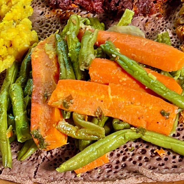 Close-up of Ethiopian injera bread topped with vibrant green beans and orange carrots.