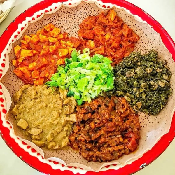 A vibrant Ethiopian platter with five distinct dishes arranged on injera bread in a red-rimmed tray.