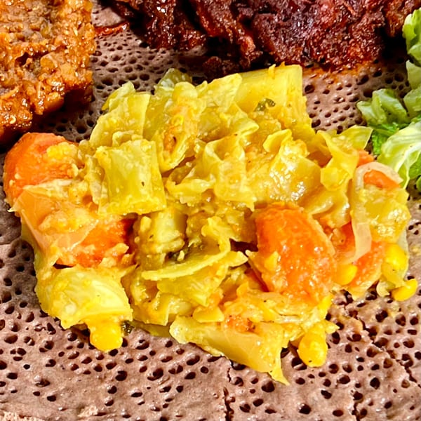 Close-up of Ethiopian injera bread topped with yellow cabbage, carrots, and corn.