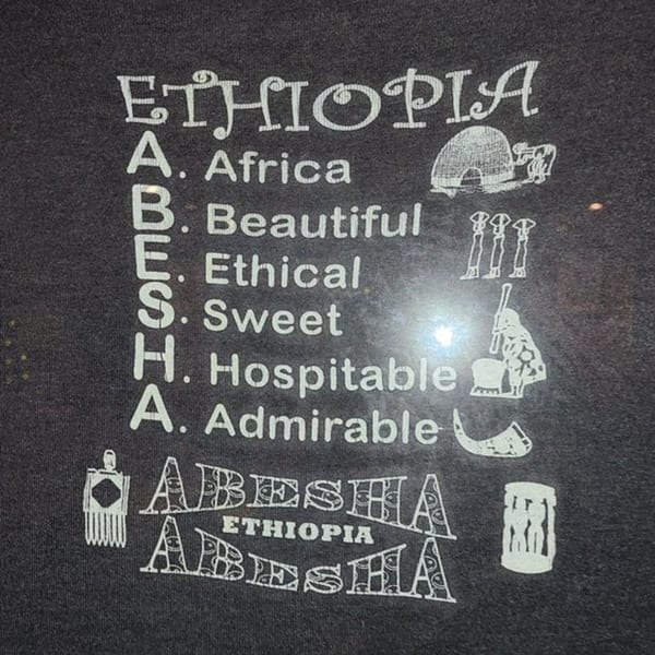 Black fabric with white text spelling "ETHIOPIA" and an acrostic for "ABESHA" with cultural illustrations.