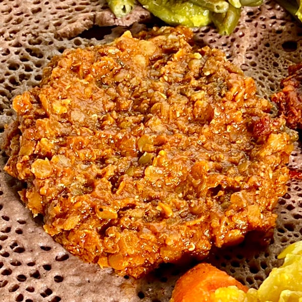 Close-up of Ethiopian misir wot (red lentil stew) on injera bread with vegetable sides.